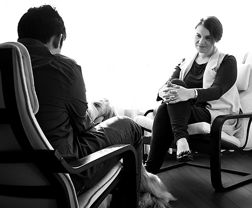 Therapist and Patient sit opposite each other. Patient pets therapy dog